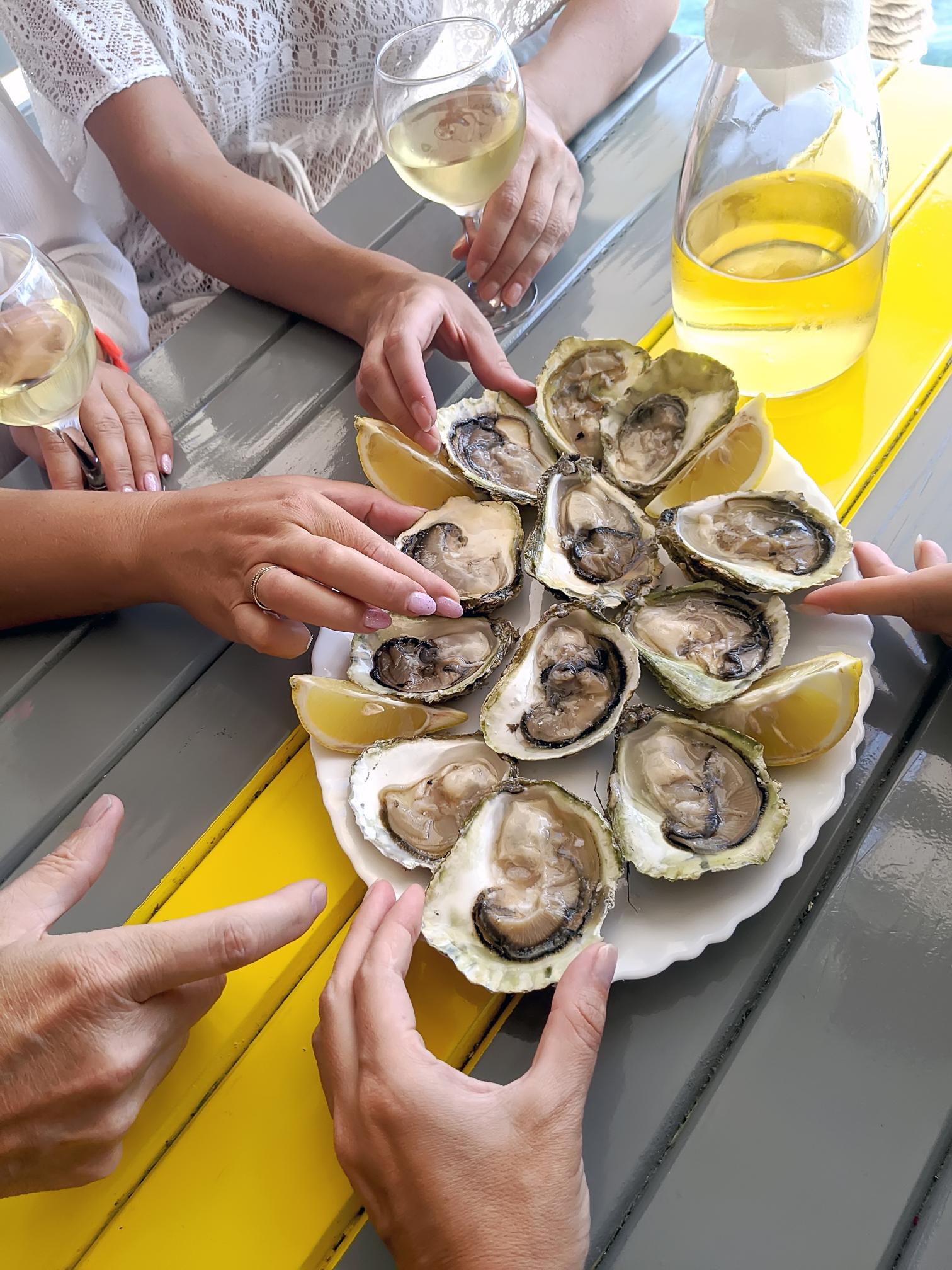 Plate of oysters and wine with people eating them