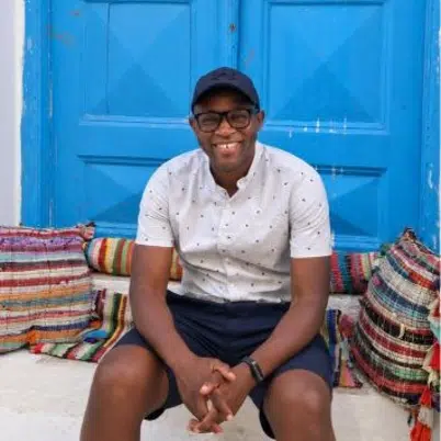 Muno Mandiza is sat outside a bright blue door