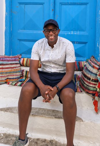 Muno Mandiza is sat outside a bright blue door